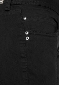 Svarta denimjeans med en närbild av fickområdet. Funktioner inkluderar silverdetaljer och en liten hjärtformad dekoration.