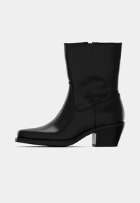 Melna ādas potīšu zābaks ar kvadrātu formas purngaliem un nedaudz paceltu blokveida papēdi. Iekļauts sānu rāvējslēdzis un gluda, spīdīga apdare.