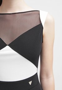 Czarna i biała sukienka z przezroczystą czarną siateczką na górze, geometrycznym blokowaniem kolorów oraz srebrnym detalem w kształcie trójkąta po boku.