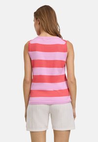 Mouwloos gebreid topje met brede roze en koraalkleurige strepen, met een ronde halslijn en een gestructureerde afwerking. Draagt met witte gestructureerde shorts.