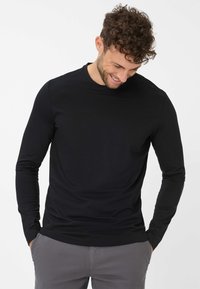 Schwarzes langärmliges T-Shirt aus leichtem, dehnbarem Stoff mit Rundhalsausschnitt und lässiger Passform, kombiniert mit hellgrauen Hosen.