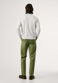 Maglione grigio chiaro con colletto rotondo, abbinato a pantaloni verde oliva e scarpe marroni. L'outfit presenta un design casual.