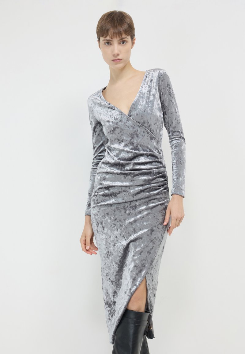 Robe en velours gris avec un décolleté en V profond, des manches longues et des fronces diagonales ; présente une fente jusqu'au genou et une silhouette ajustée.