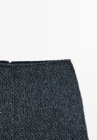 Närbild av texturerad marinblå stickad tyg med små vita prickar och ett ribbat mönster längs kanten, troligtvis en del av ett plagg.