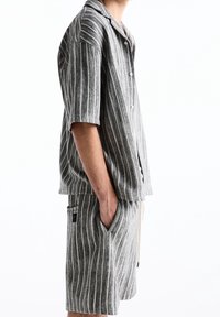 Ensemble composé d'une chemise à manches courtes rayée et d'un short dans des tons gris, présentant une fermeture boutonnée, des poches plaquées et une coupe décontractée avec un tissage texturé.