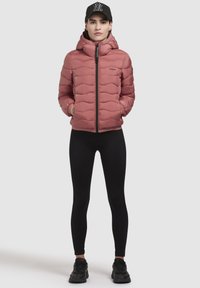 Pink puffer jacket with a hood, quilted pattern, front zipper, and two side pockets. Worn with black leggings and black sneakers.