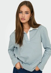 Polo de manga larga, color azul claro, con cuello blanco y finas rayas horizontales en azul oscuro y gris. Tejido suave, corte relajado.