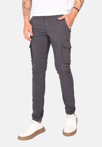 Pantaloni cargo grigi con una vestibilità slim, dotati di tasche laterali e un tessuto liscio, leggermente texture. Abbinati a sneaker bianche.