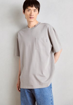 Lys grå t-shirt, rund hals, korte ærmer, afslappet design, med en venstre brystlomme med diskret syningsdetalje.