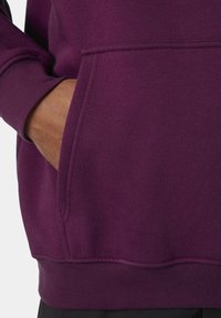 Sudadera morada con un bolsillo tipo canguro, que presenta una textura suave y puños acanalados. El dobladillo está acabado de forma ordenada, mostrando un ajuste relajado.