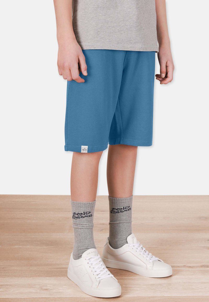 Blå sportshorts med elastisk midja, ihopparat med grå strumpor och vita sneakers. Shortsen har en liten logotypetikett på fållen.