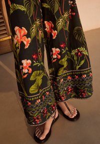 Pantaloni negri cu imprimeu floral, având modele vibrante de roz și verde, cu broderie într-o manieră sofisticată la tiv și sandale negre cu bretele.