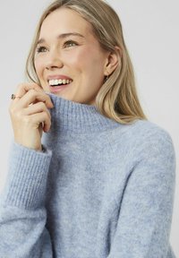 Pull bleu clair avec un col côtelé haut et des poignets côtelés, fabriqué à partir d'un tissu texturé doux, présentant une coupe décontractée et un design minimaliste.