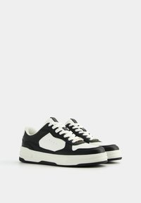 Black and white leather sneakers with a rounded toe, white laces, and a textured sole. Notable side panel detail and stitching.