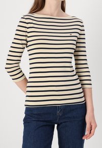 Pruhovaný bavlněný top s námořnickými a krémovými vodorovnými pruhy, lodičkovým výstřihem, tříčtvrtečními rukávy a malým logem na hrudi.