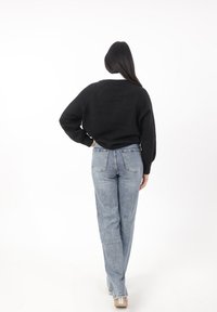 Maglione nero a maniche lunghe con una vestibilità comoda, abbinato a jeans a gamba dritta di colore azzurro chiaro. I jeans presentano tasche posteriori e una finitura sbiadita.