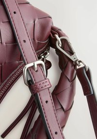 Burgunderfarbene handgewebte Lederhandtasche mit strukturiertem Finish, silbernem Hardware, verstellbarem Tragegurt und Reißverschlussdetails. Nahaufnahme der Gurverbindung.