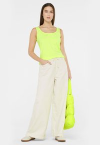 Neon green tank top and beige wide-leg pants, with a textured, puffy green handbag. The top has a square neckline and side pockets.