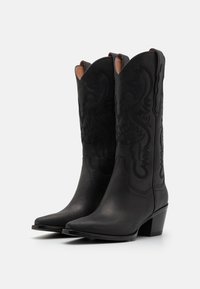 Sorte lær cowboy støvler med spidse tæer, dekorativ syning og en stablet hæl. Har buede toppe og indviklet prægede detaljer.