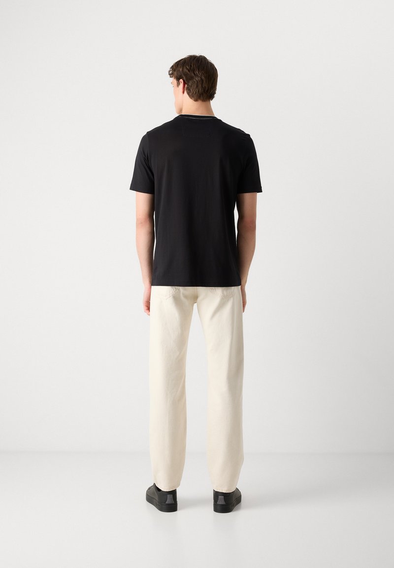 T-shirt noir à manches courtes en tissu doux, associé à un pantalon beige clair ; design simple sans motifs ni graphiques visibles.