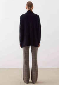 Czarny, oversize'owy sweter z golfem, zestawiony z wysokim stanem, szerokimi spodniami w kratę. Gładka faktura i luźny fason.