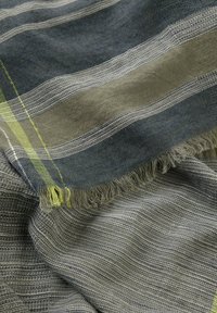Vævet tekstil med horisontale striber i mørkeblå og lys grå, med frynsekant og en subtil limegrøn accent. Blød tekstur.