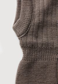 Strikket brunt stoff med en teksturert, ribbet design. Har en tettsittende passform og jevn detaljering gjennom hele. Nærbilde av materialet.