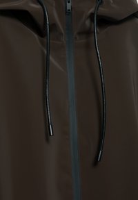 Geacă cu glugă maro închis, cu fermoar frontal negru și șnururi negre cu capete acoperite.