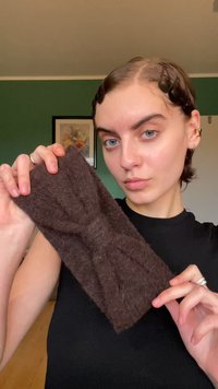 Fascia in felt marrone con un dettaglio a fiocco frontale, superficie testurizzata e colore uniforme, tenuta da una persona in una maglietta nera, con mani visibili.