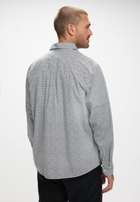 Camisa de manga larga con cuello en un patrón geométrico blanco y negro, que presenta una espalda plisada y puños con botones. Tejido texturizado, ajuste relajado.