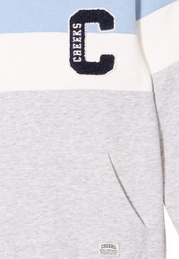 Felpa grigia chiaro con strisce orizzontali blu e bianche. Presenta un logo "C" ricamato e una tasca frontale. Tessuto morbido e strutturato.