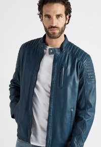 Blauwe leren jas met een gladde textuur, voorzien van doorgestikte schouderdetails, een staande kraag en een ritsborstzak.