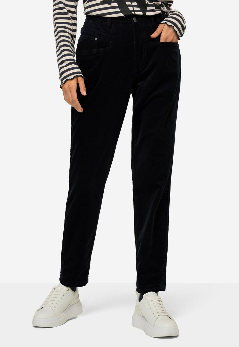Marineblauwe corduroy broek met een rechte pijp, voorzien van voorzakken en een knoopsluiting, gecombineerd met witte sneakers en een gestreept shirt.
