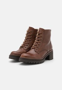 Stivali ankle in pelle marrone con punta rotonda, lacci frontali e suola texturizzata. Presentano un tacco basso a blocco e dettagli di cucitura discreti.
