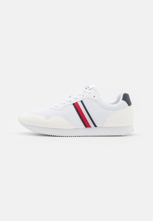 Białe buty sportowe z teksturowanej tkaniny, z czerwonymi i granatowymi paskami. Okrągły czubek, biała gumowa podeszwa i sznurowany design.