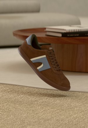 Brauner Wildleder-Sneaker mit hellblauen Akzenten, rundem Zehenbereich, brauner Sohle und weißen Details. Schnürsenkel und ein gepolsterter Kragen sorgen für Komfort.