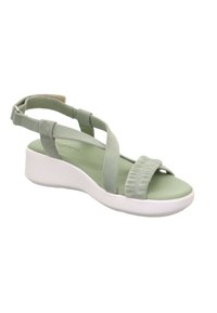 Zielone zamszowe sandały z krzyżującymi się paskami, wyściełanym wnętrzem i białą podeszwą na koturnie, z akcentem w postaci pierścienia na pasku z tyłu.