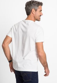T-shirt bianca a maniche corte con collo rotondo, realizzata in tessuto morbido, abbinata a jeans in denim scuro, vista da dietro.