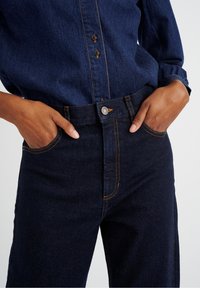 Donkerdenimjeans met oranje stiksels, voorzien van een knoopsluiting, voorzakken en een ontspannen pasvorm bij de taille en de dijen.