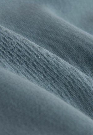 Mjuk, texturerad tyg i en dämpad blå nyans, med fina vävda mönster och en slät yta, arrangerad i mjuka veck.