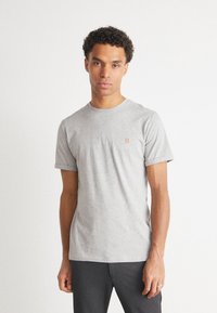 Camiseta gris de manga corta hecha de una tela suave. Presenta un cuello redondo y un pequeño logo bordado en naranja en el pecho. Corte holgado.
