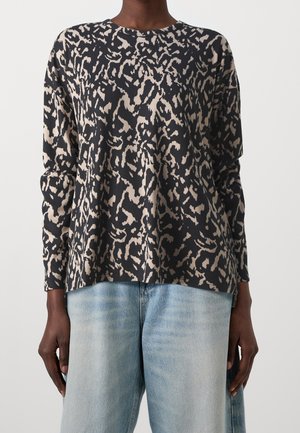 Zwart-beige gebreide trui met lange mouwen, gemaakt van zachte stof, met een ronde hals en een losse pasvorm, gecombineerd met lichtblauwe spijkerbroek.