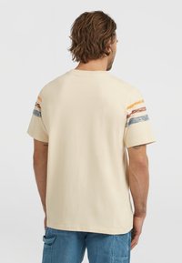 Beige pamut póló, rövid ujjakkal, narancssárga, piros és kék vízszintes csíkokkal a vállakon. Klasszikus kerek nyakkivágású.