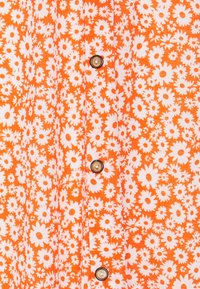 Tissu à motif floral orange comprenant de petites marguerites blanches, avec des boutons ronds marron sur le devant. Conçu avec une texture douce et légère.