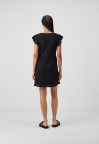 Robe noire courte avec des manches courtes à volants, tissu texturé, taille cintrée et ourlet avec des découpes, associée à des sandales noires.