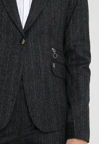 Tmavě šedý blazer s proužkovaným vzorem, se zapínáním na knoflík, boční kapsou na zip a texturovaným detailem na manžetách.