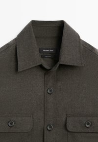 Mørkegrøn, textured skjorte med en krave der knappes op, to brystlommer og sorte knapper. Mærket siger "Massimo Dutti."