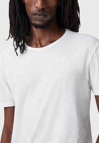 T-shirt bianco a maniche corte con scollatura rotonda, realizzato in un tessuto testurizzato che mostra sottili variazioni. Presenta una vestibilità comoda e cuciture pulite.