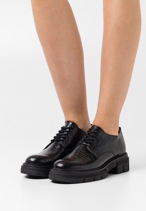 Chaussures en cuir noir à lacets avec une finition texturée, dotées d'une semelle épaisse noire et d'un design à bout rond.