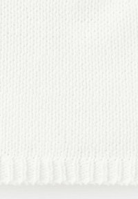 Gros plan d’un tissu en tricot blanc montrant des points côtelés verticaux et horizontaux avec un motif texturé.